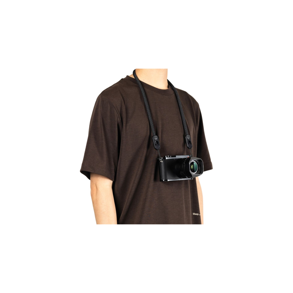 Een persoon in een bruin t-shirt draagt een zwarte camera met een gevlochten riem.