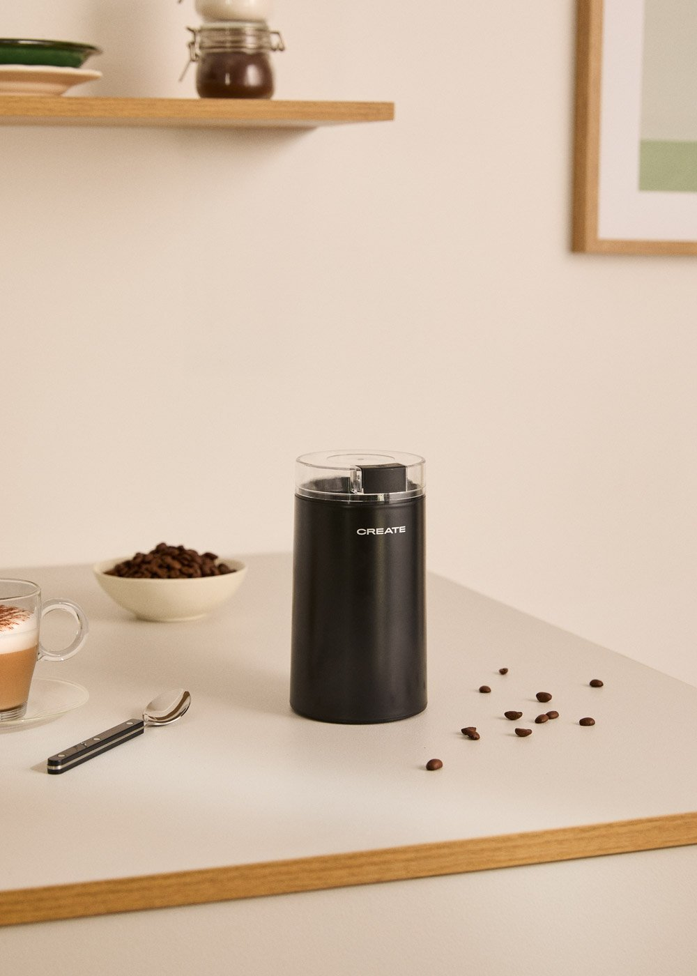Trituradora de café negra con granos de café, taza y cuchara.