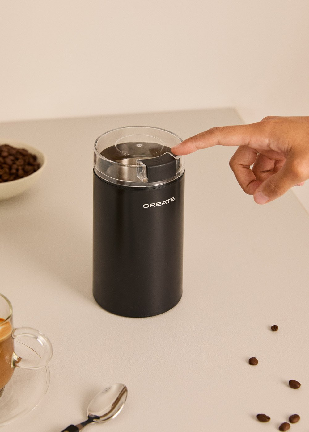Un molinillo de café negro con tapa transparente, presionado por un dedo.