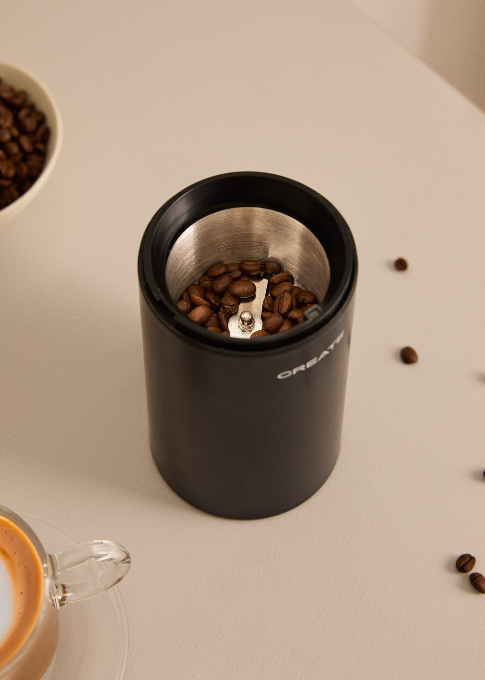 Un molinillo de café negro con granos y una taza de café al lado.