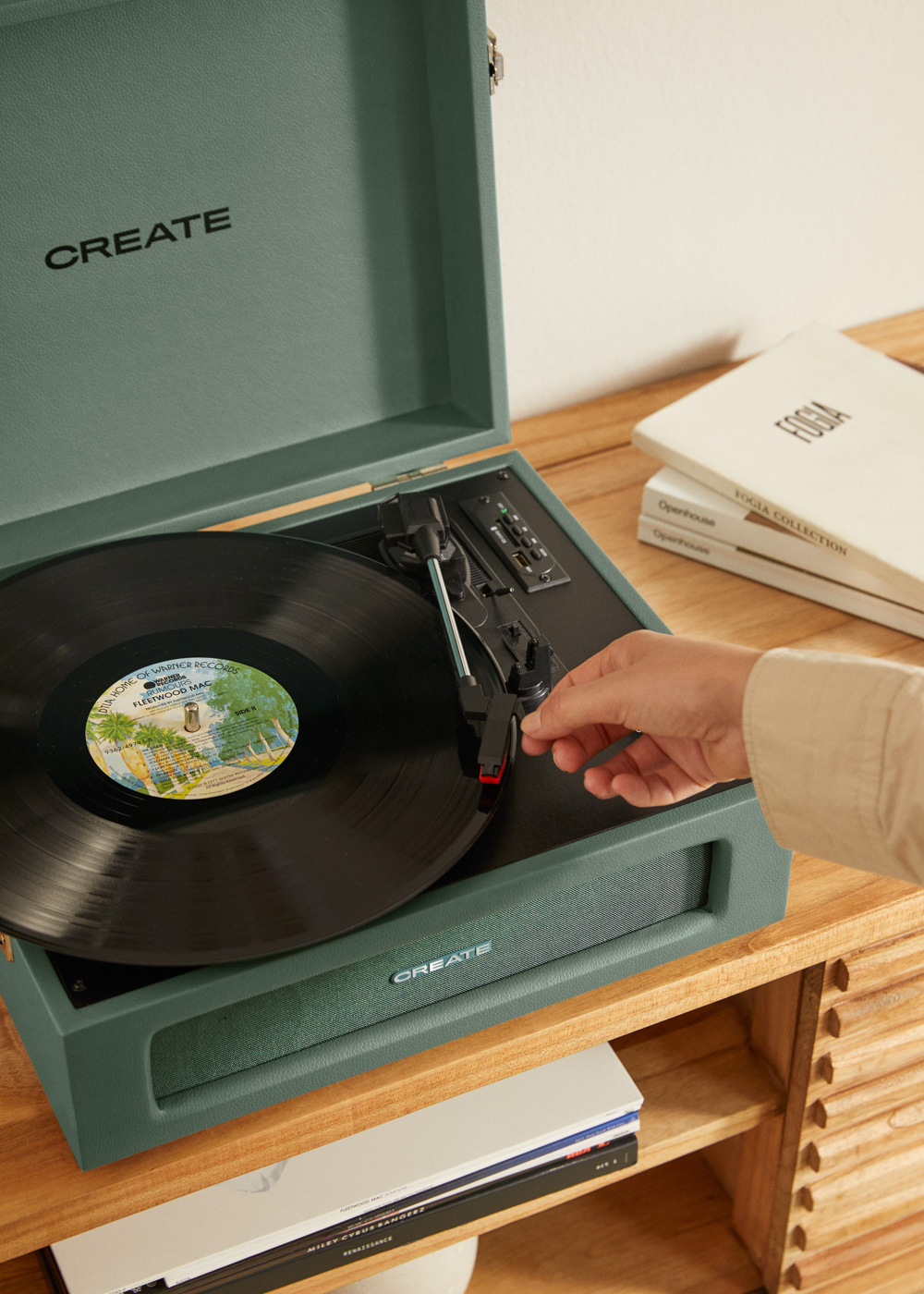 Una mano baja la aguja de un tocadiscos verde con un disco de Fleetwood Mac.