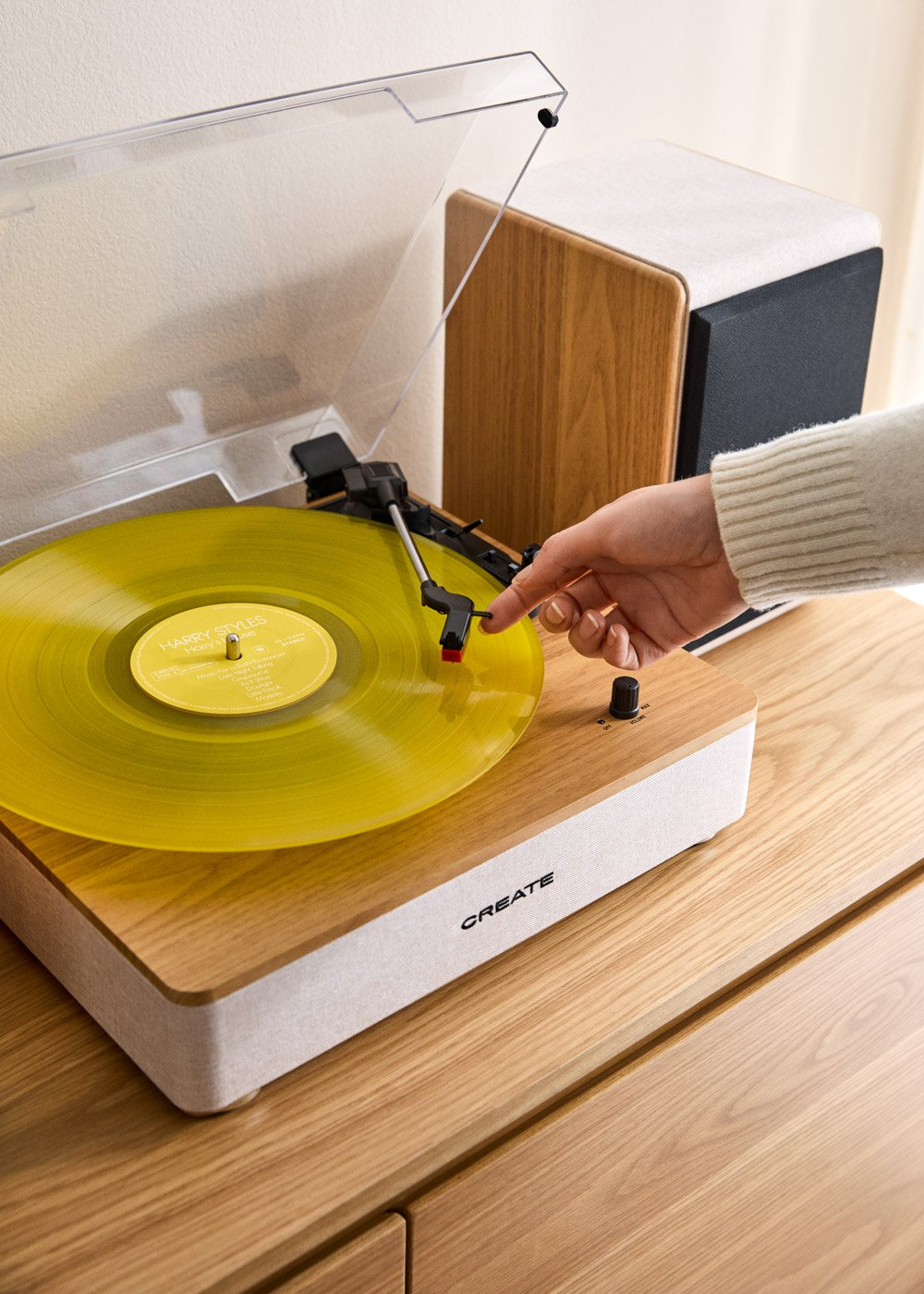Una mano coloca un disco de vinilo amarillo en un tocadiscos de madera junto a un altavoz.