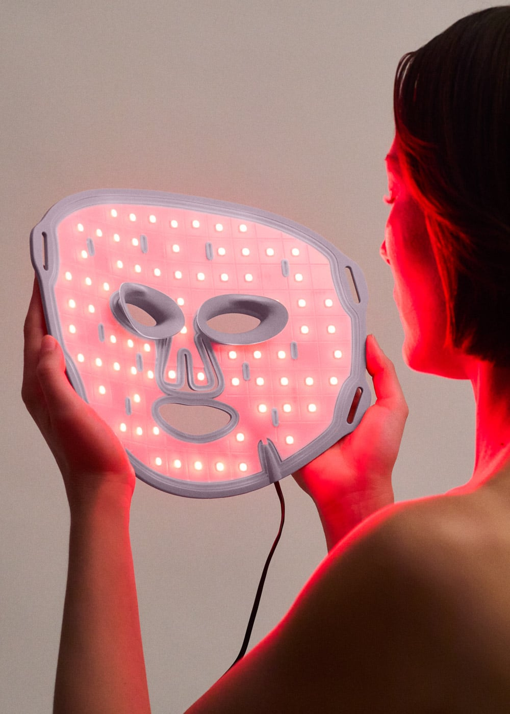 Una persona sostiene una mascarilla con luces LED rojas frente a su cara.