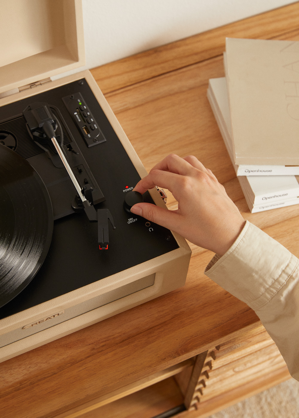 Una mano gira el control de volumen de un tocadiscos en una mesa de madera.