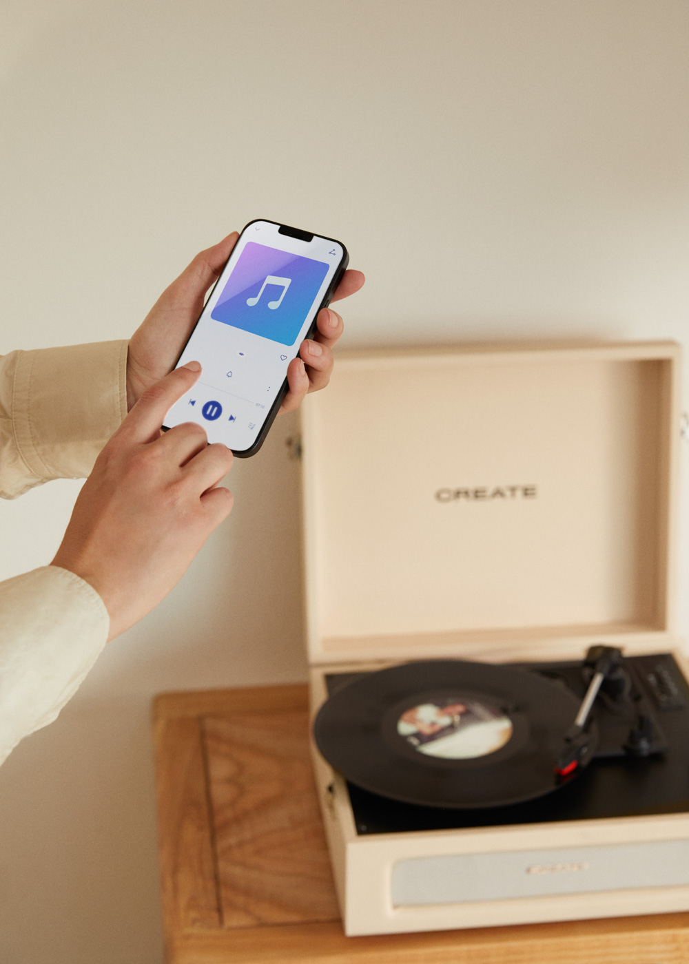 Una mano sostiene un smartphone con una app de música junto a un tocadiscos.