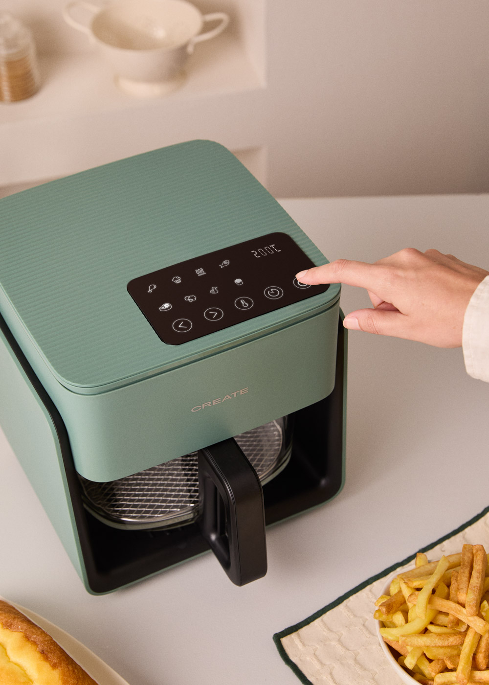 Freidora de aire verde con pantalla de 200°C. Una mano opera los controles.