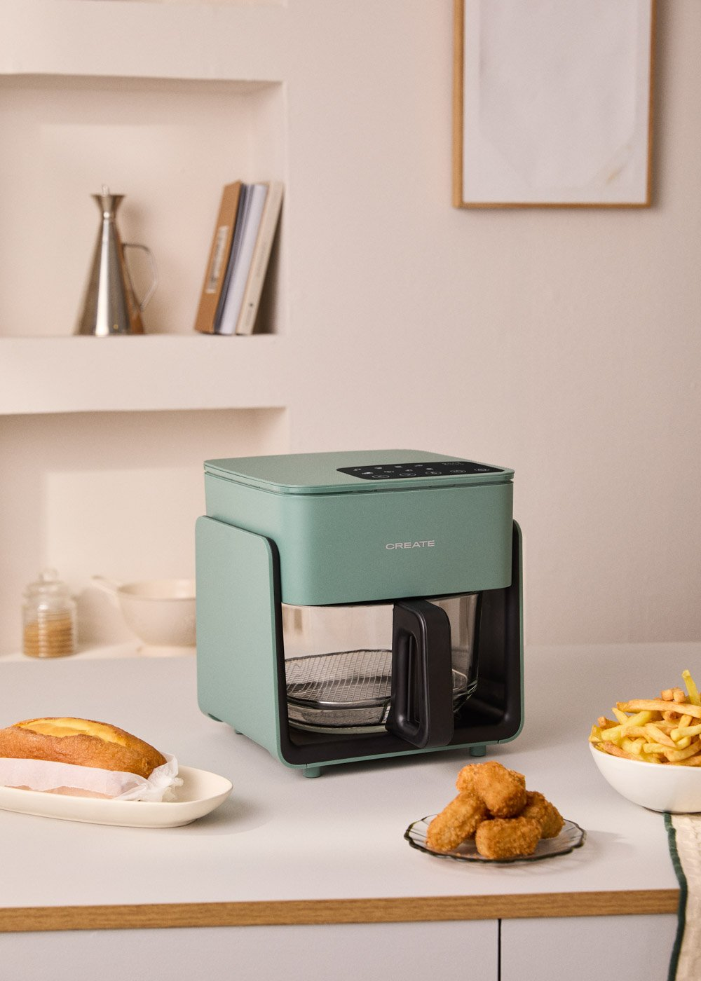 Una freidora de aire verde está sobre un mostrador con pan, nuggets y patatas fritas.