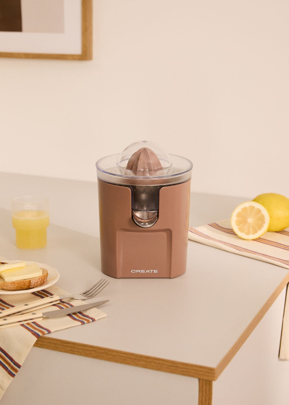 Un exprimidor de cítricos rosa está sobre una mesa con un vaso de jugo, tostada y limones.