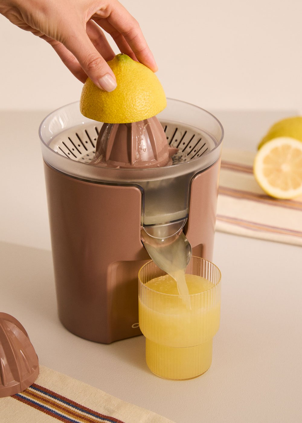 Una mano presiona un limón sobre un exprimidor. El jugo fluye hacia un vaso.