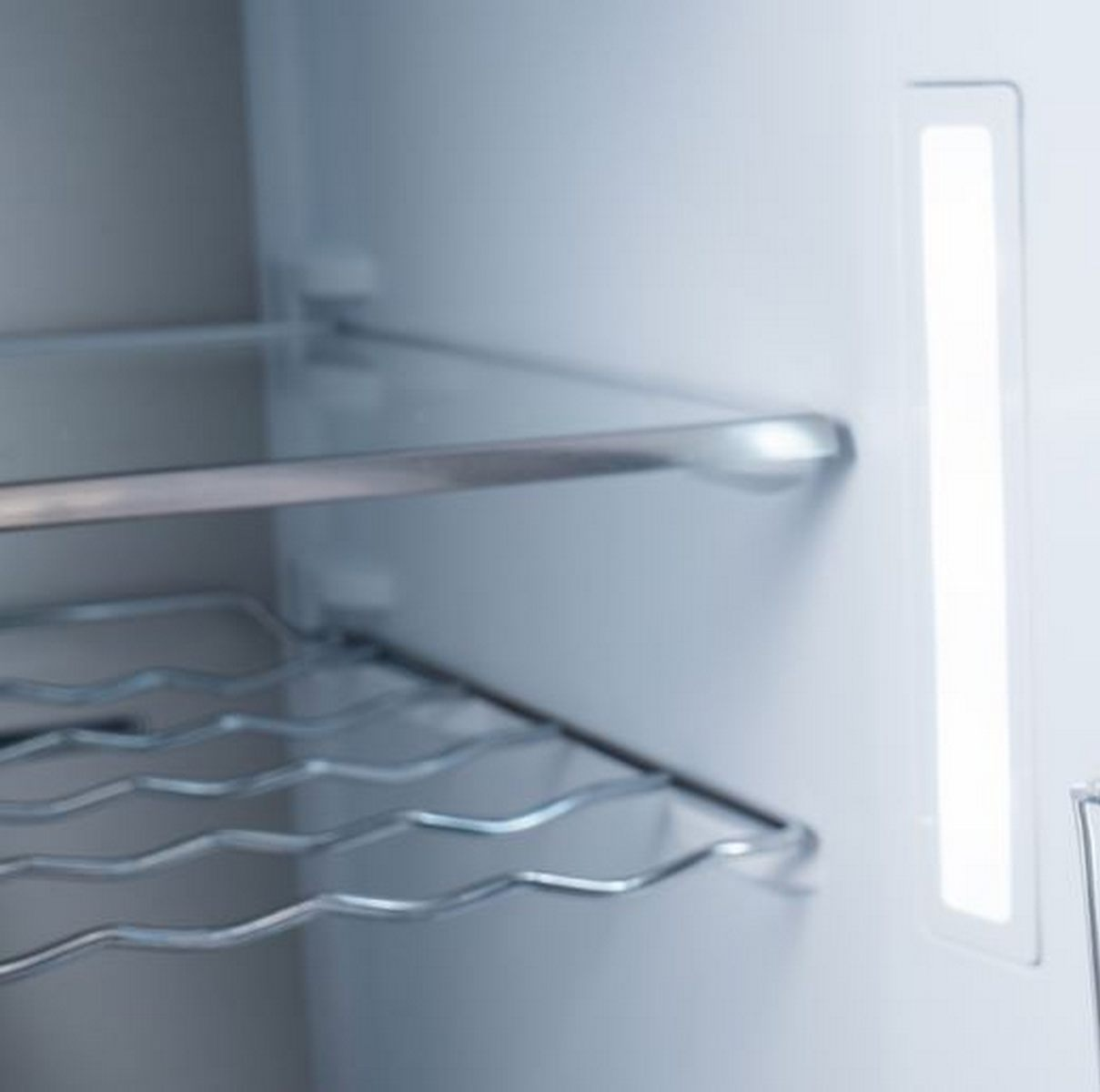 Compartimento de frigorífico vacío con estante de alambre y tira de luz.