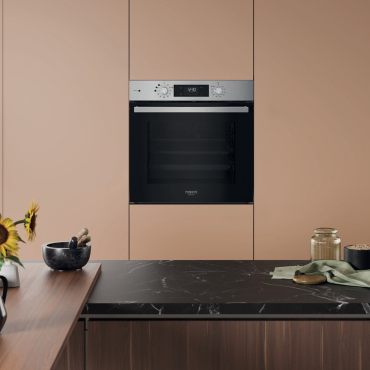 Un forno da incasso moderno in una cucina con mobili color pesca e piano di lavoro in marmo.