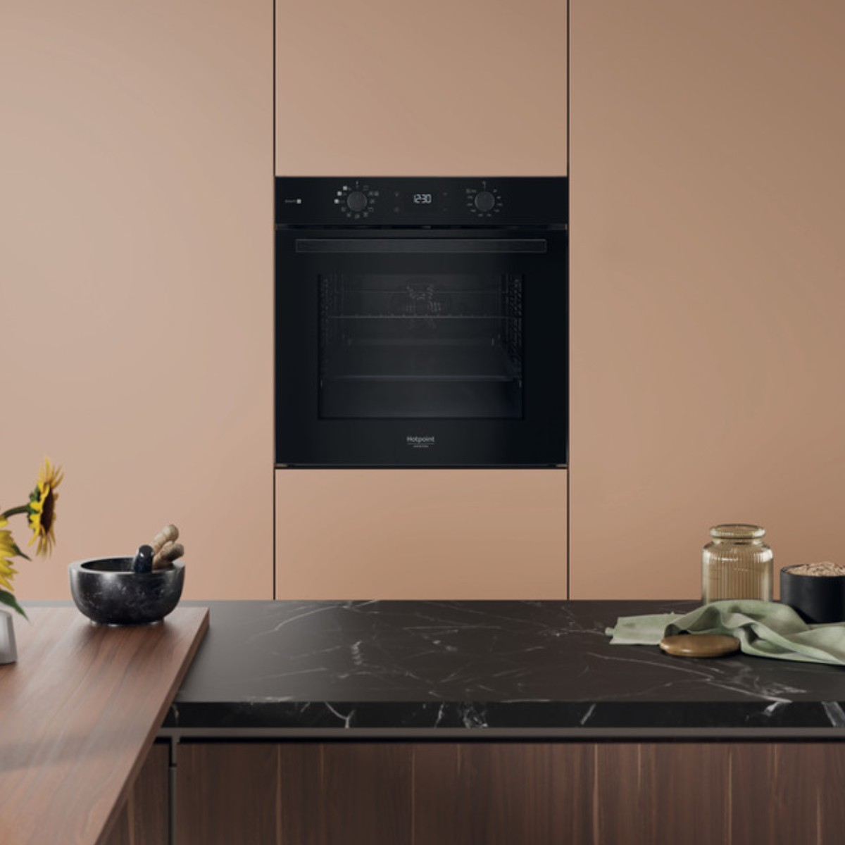 Un forno nero moderno è installato in una cucina color pesca. Un piano di lavoro in marmo presenta decorazioni.