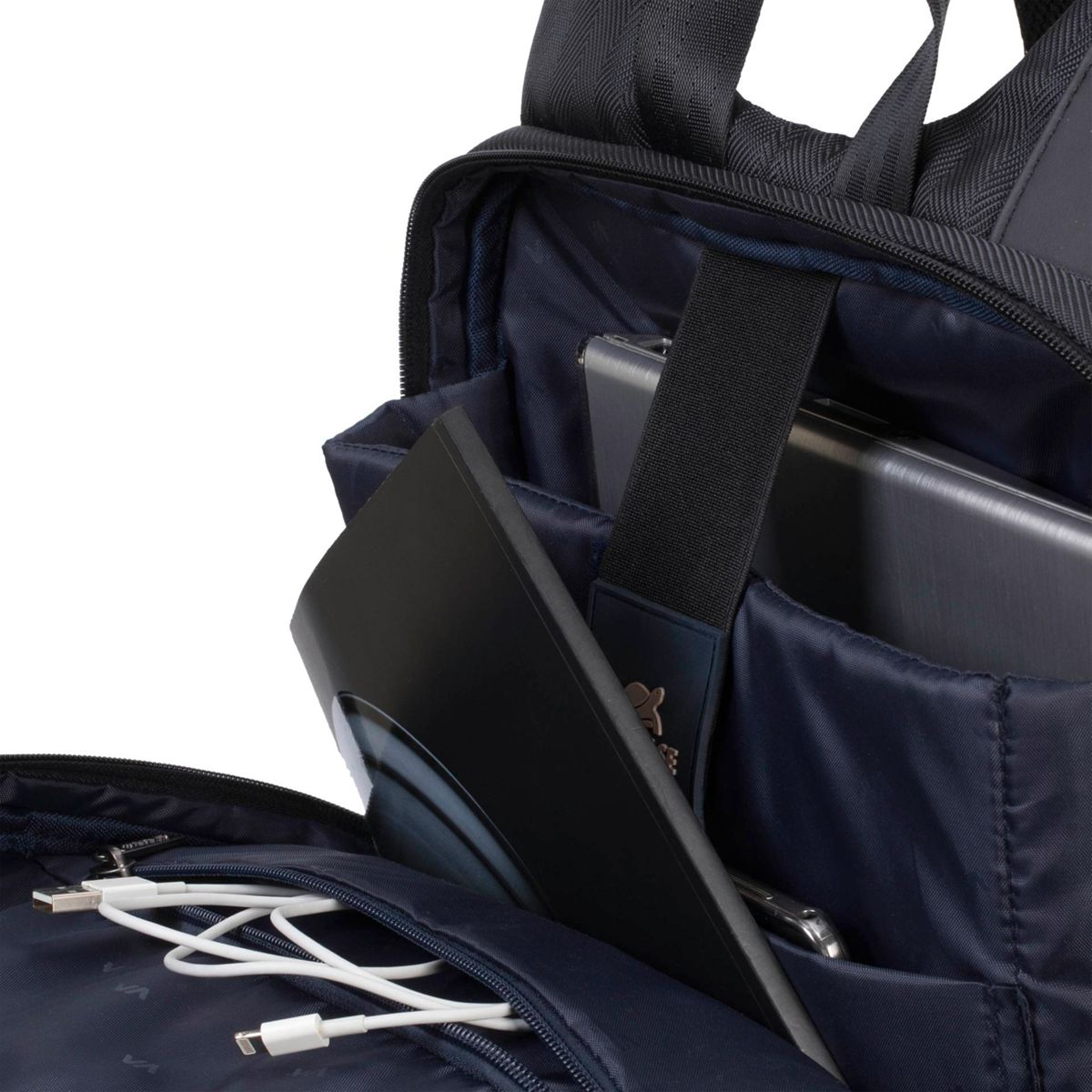 Innenansicht eines dunkelblauen Rucksacks mit Laptop, Tablet und weißen Ladekabeln.