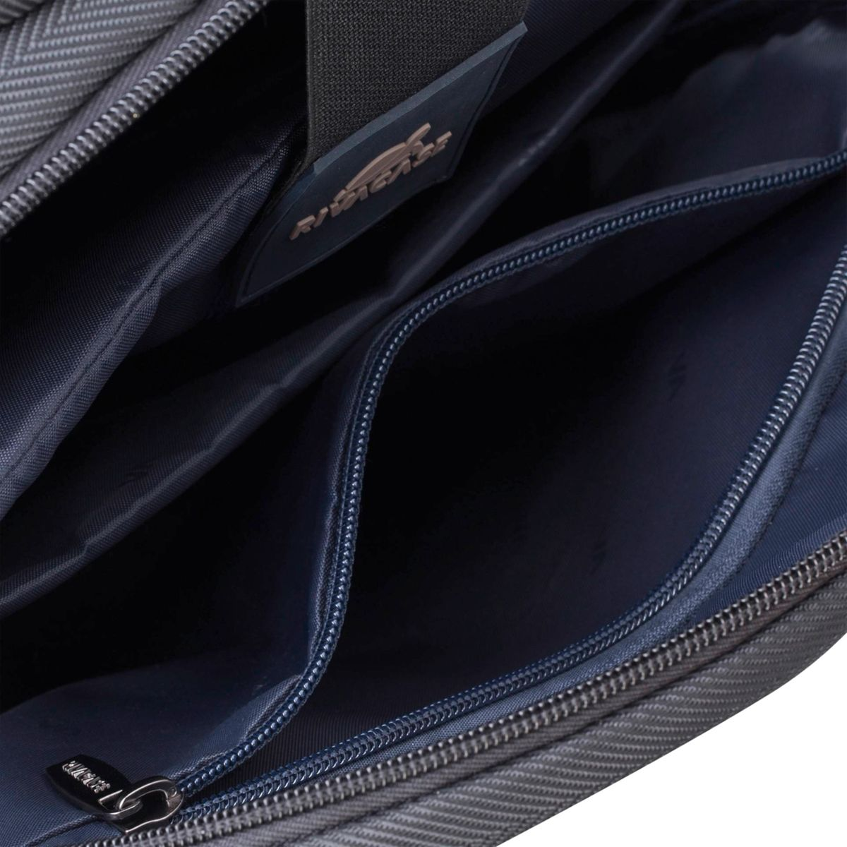 Nahaufnahme des offenen Innenraums einer grauen Tasche mit dunkelblauer Auskleidung und Reißverschlusstaschen.