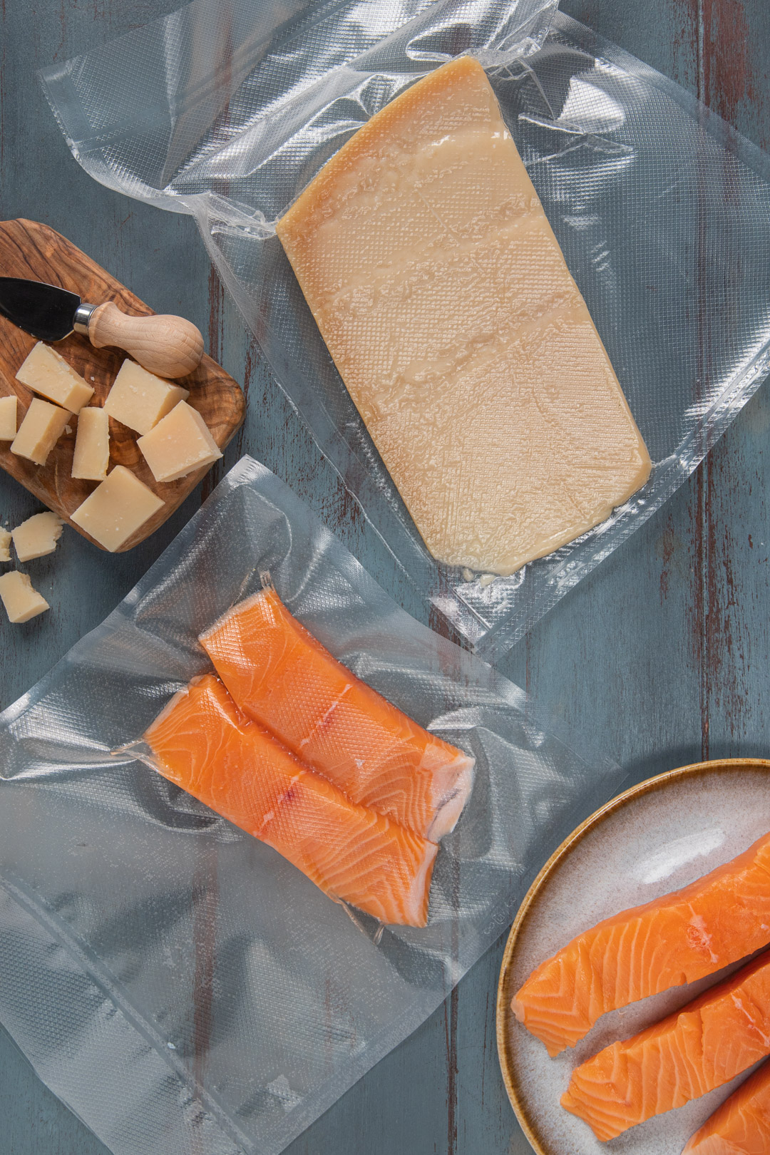 Queso y salmón envasados al vacío sobre fondo de madera azul.