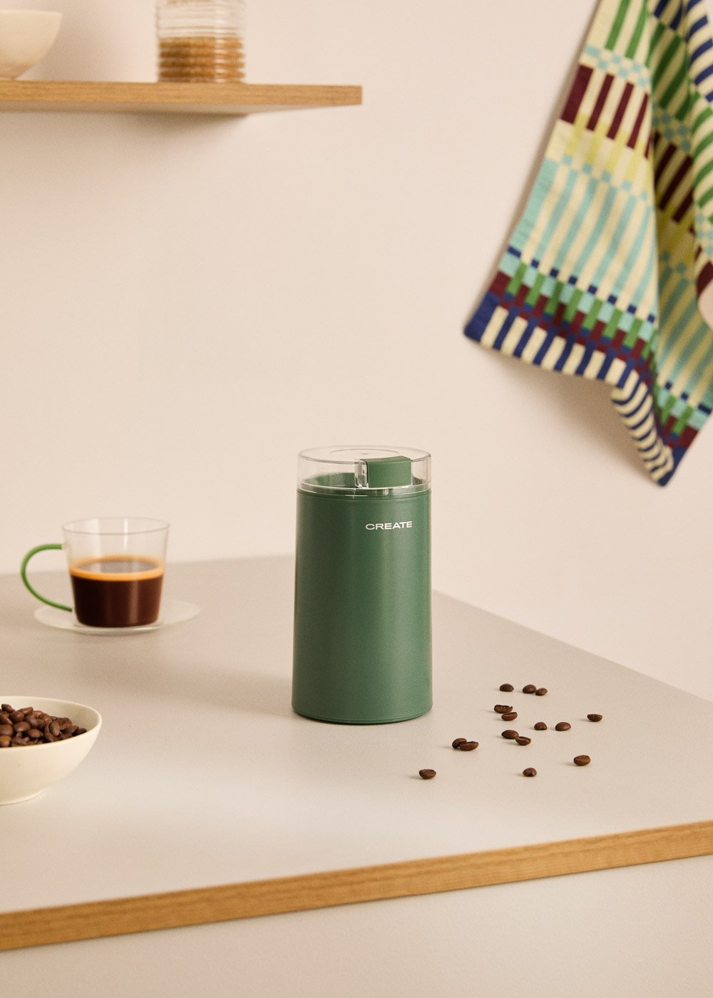 Molinillo de café verde junto a taza de espresso y granos de café en mesa.