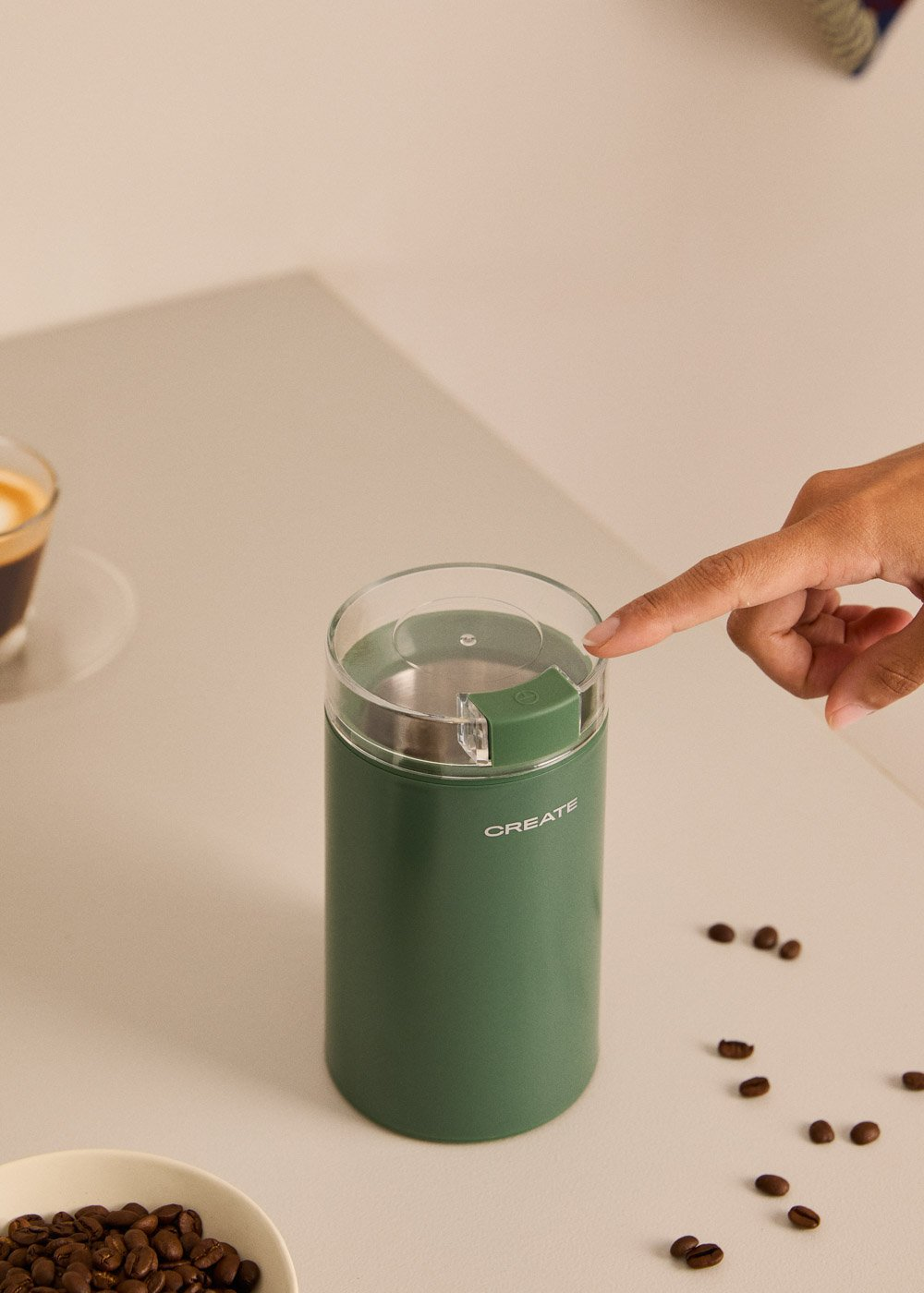 Un molinillo de café verde con un vaso de espresso al lado, sobre una mesa.