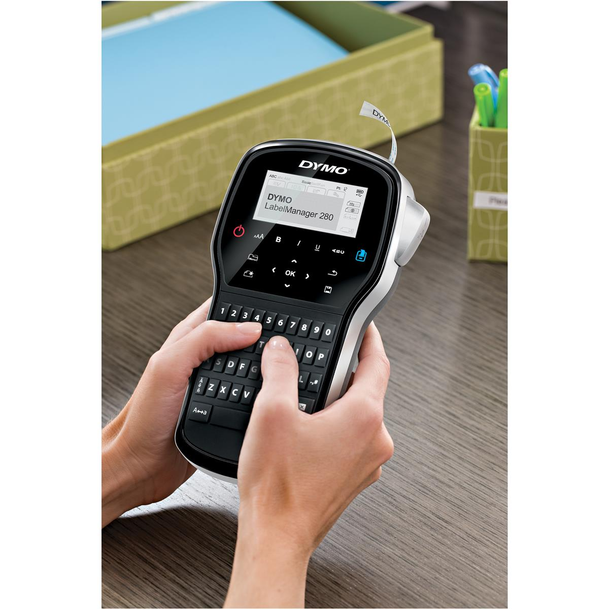 Una persona tiene una etichettatrice DYMO LabelManager 280 su un tavolo di legno.