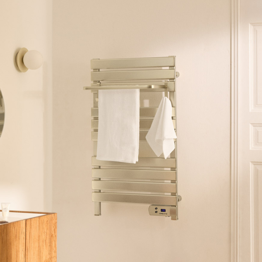 Un toallero plateado con dos toallas blancas, una lámpara de pared y un mueble de tocador de madera.