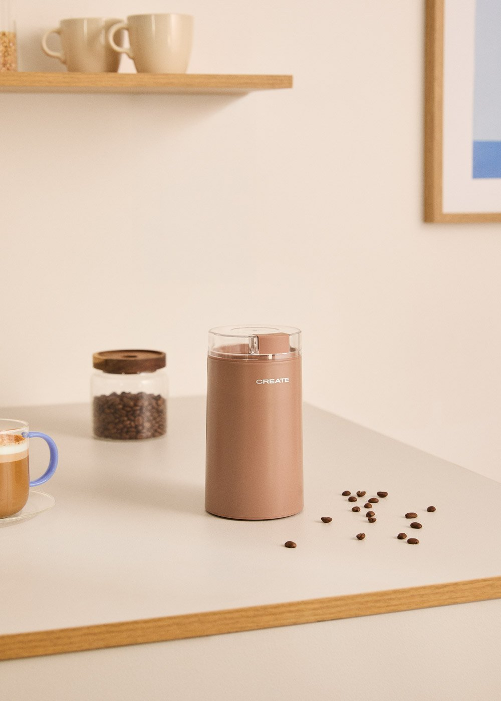 Un molinillo de café marrón con un frasco de granos de café y una taza de café.