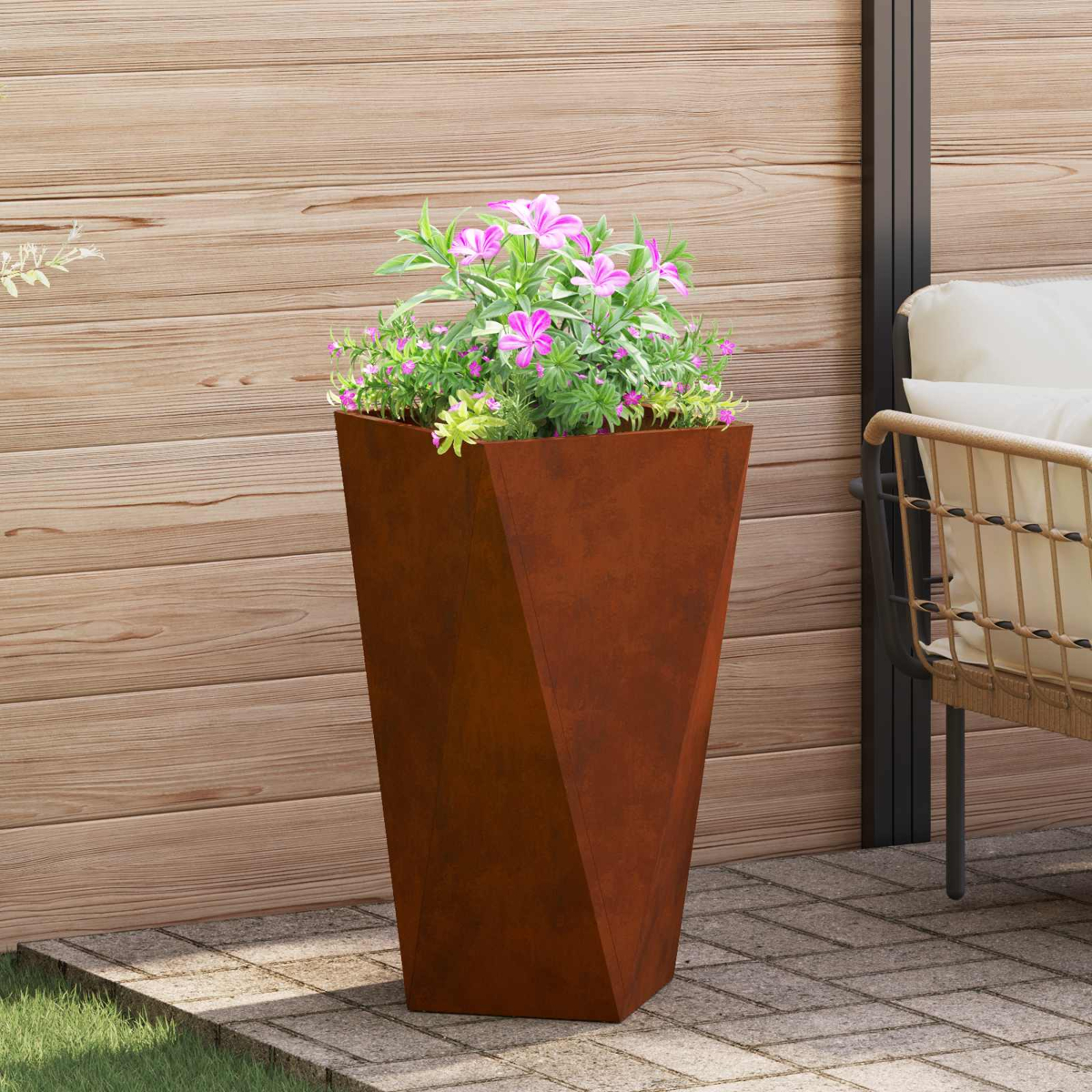 Una fioriera marrone ruggine con piante rosa e verdi si trova su un patio.