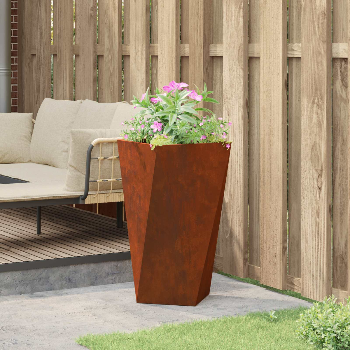 Una fioriera geometrica arrugginita con fiori rosa davanti a una recinzione di legno.