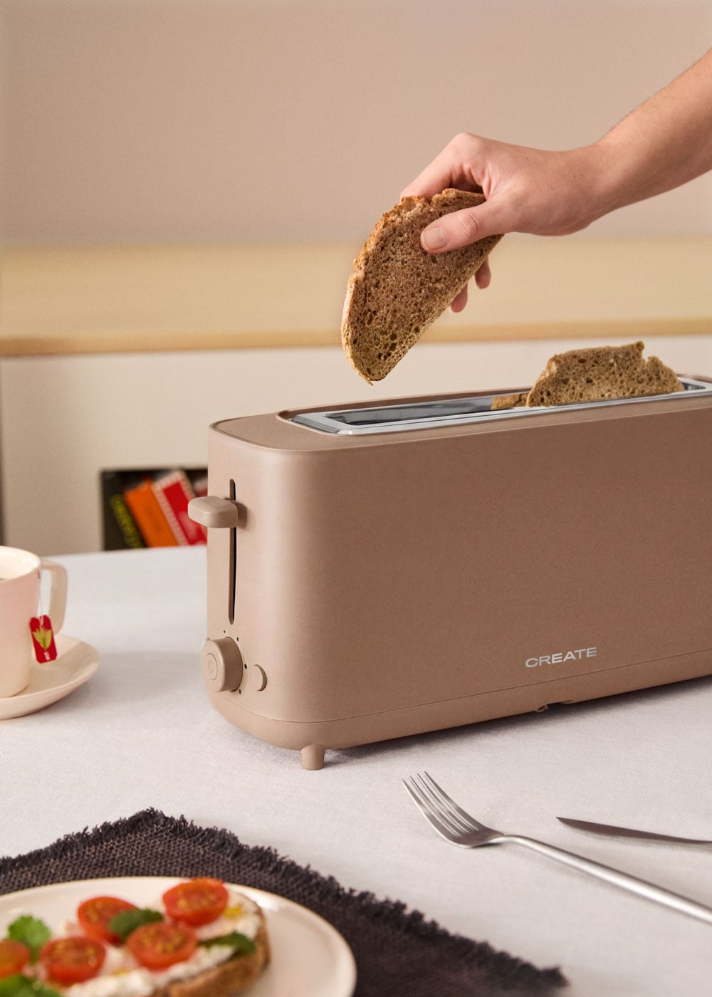 Una mano coloca una rebanada de pan en una tostadora beige. Ya hay dos rebanadas dentro.