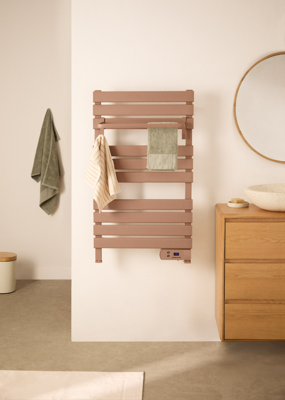 Un toallero rosa con dos toallas, junto a un espejo y un mueble de madera.