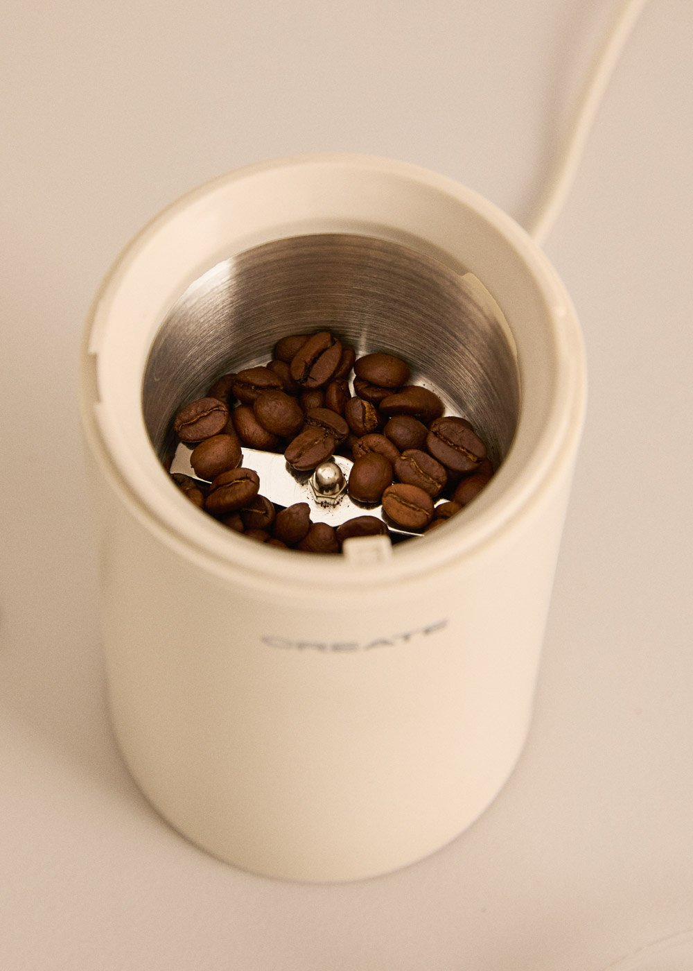 Un molinillo de café lleno de granos de café tostados oscuros, vista superior.