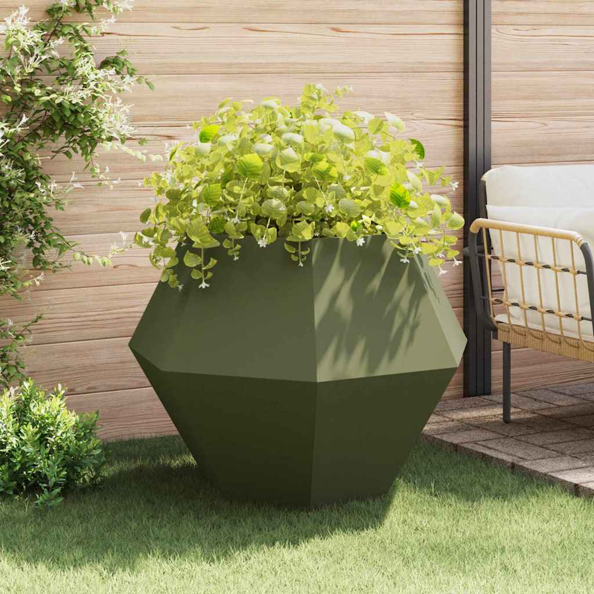 Un fioriera verde sfaccettata con piante verdi rigogliose si trova sull'erba all'aperto.