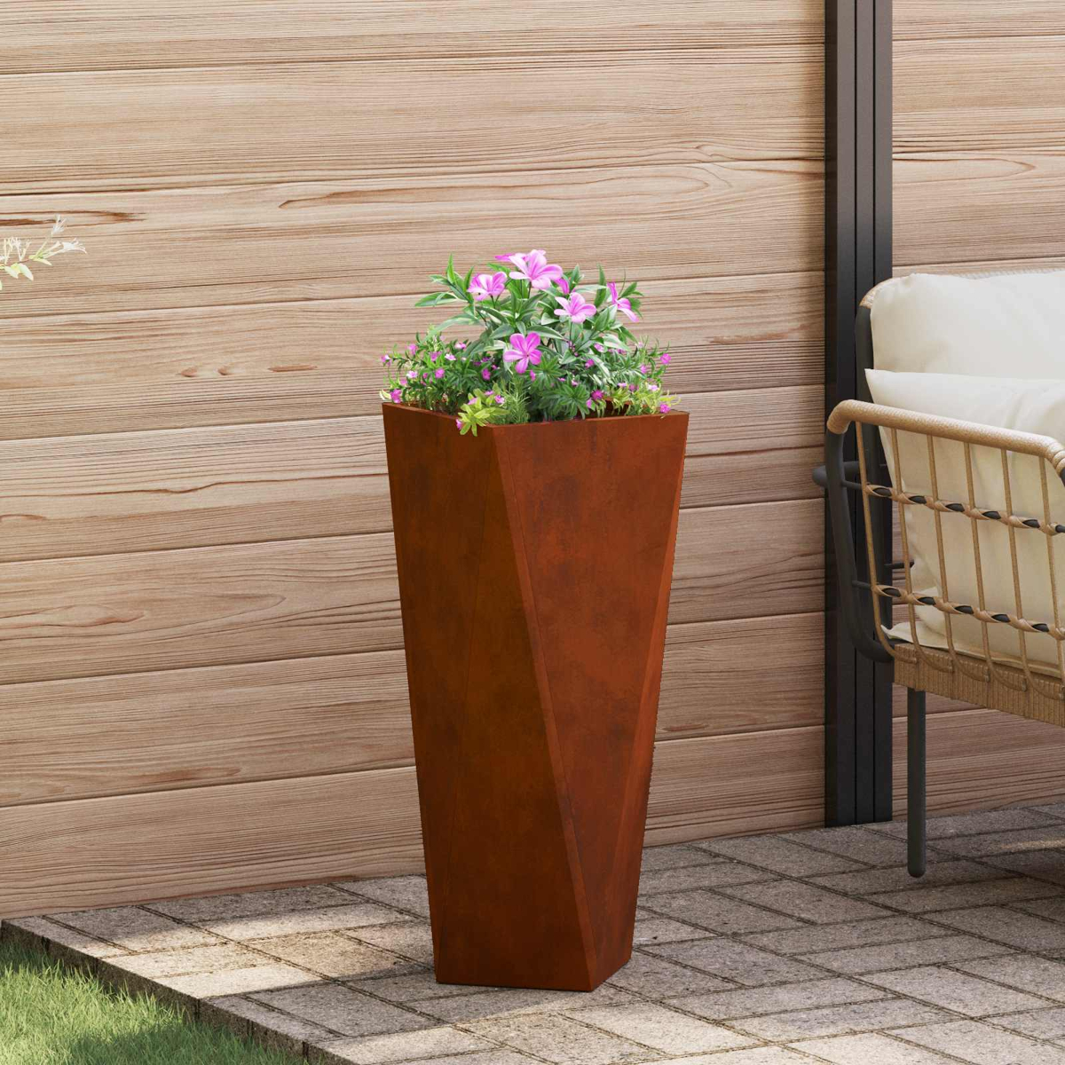 Un alto vaso color ruggine con fiori rosa su un patio accanto a un muro di legno.