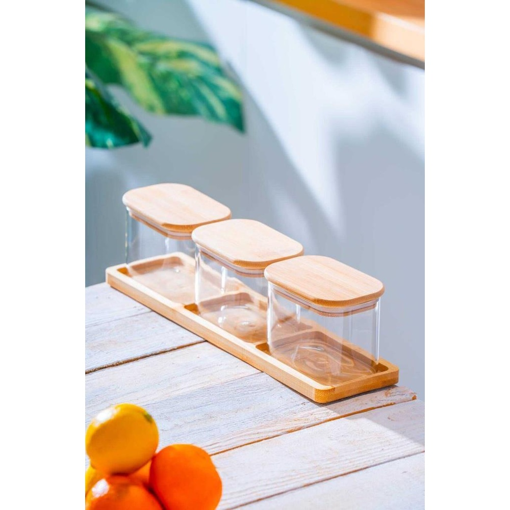Bambu kapaklı üç cam kavanoz ahşap tepside, yanında portakal ve limonlar.