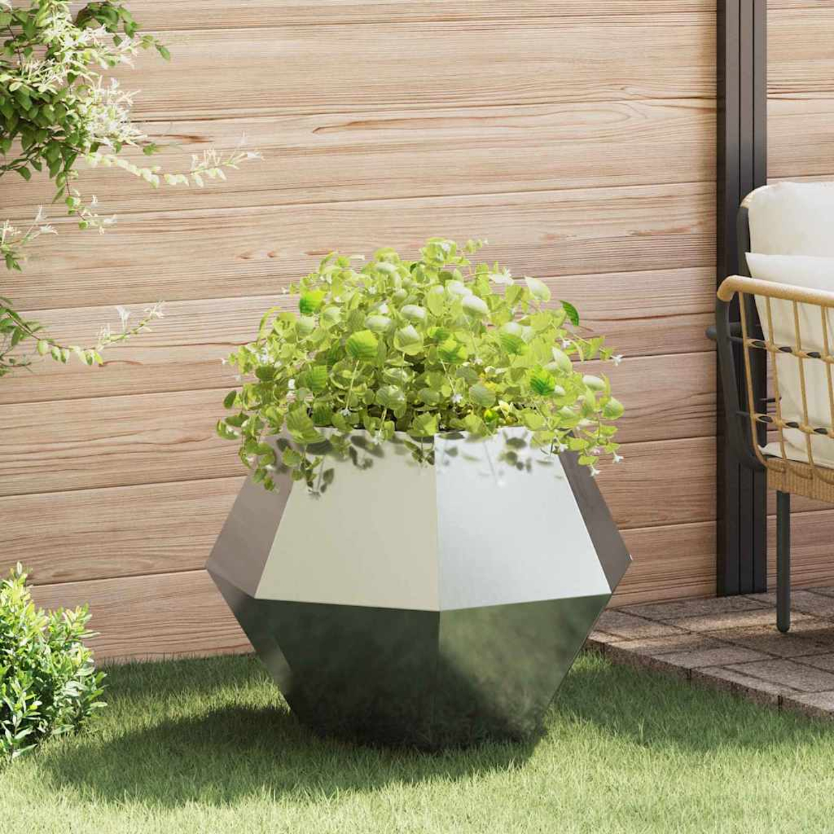 Una fioriera geometrica con piante verdi siede sull'erba davanti a un muro di legno.
