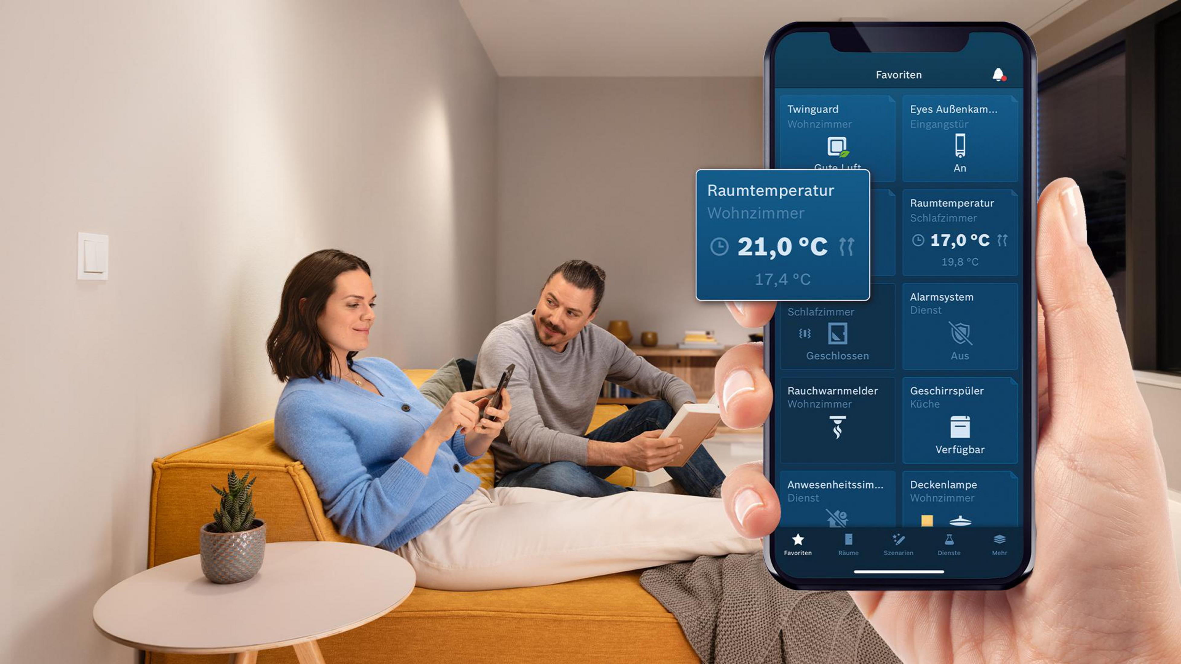 Ein Mann und eine Frau sitzen auf einem Sofa und benutzen ihre Smartphones. Eine App zeigt Smart-Home-Daten an.