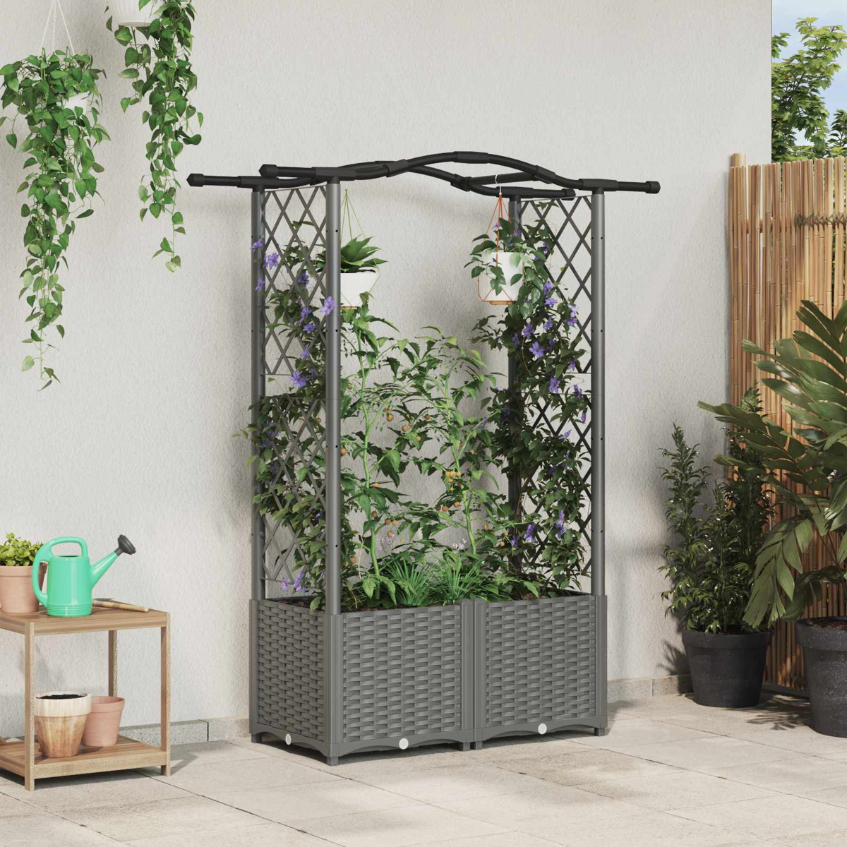 Ein grauer Gartenpflanzer mit Rankgittern, der grüne Pflanzen und lila Blumen hält.