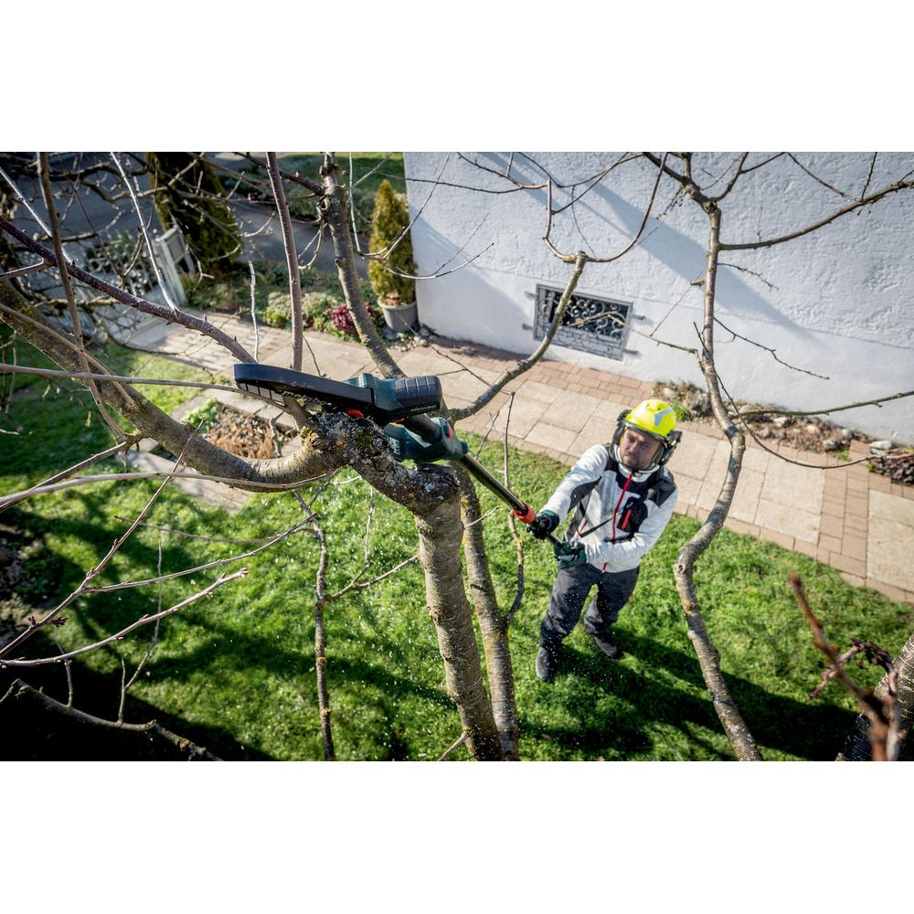 Uomo con elmetto e occhiali taglia ramo d'albero con motosega giardino.