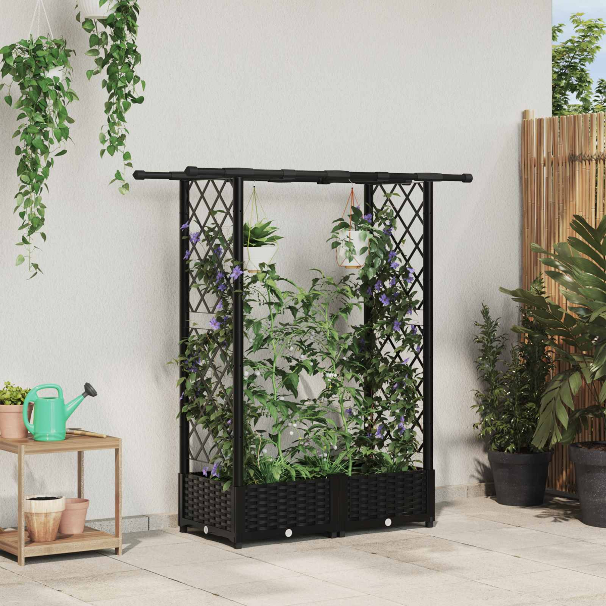 Ein schwarzes Rankgitter mit Pflanzen und Blumen auf einer Terrasse.