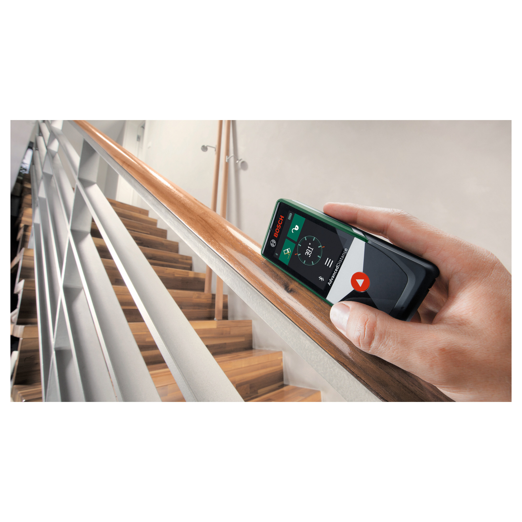 Main tenant un appareil de mesure Bosch vert sur un escalier en bois.