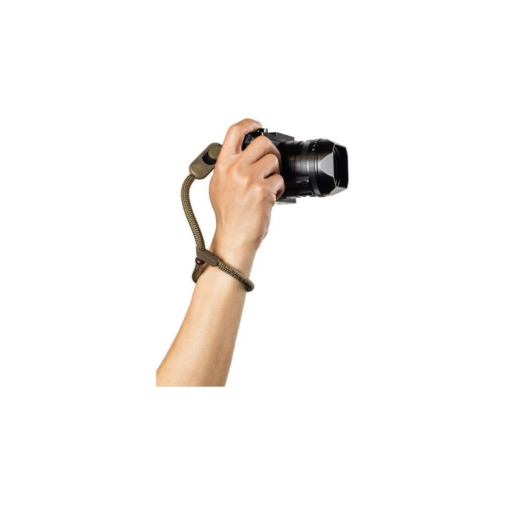 Een hand houdt een zwarte camera vast met een olijfgroene polsband.