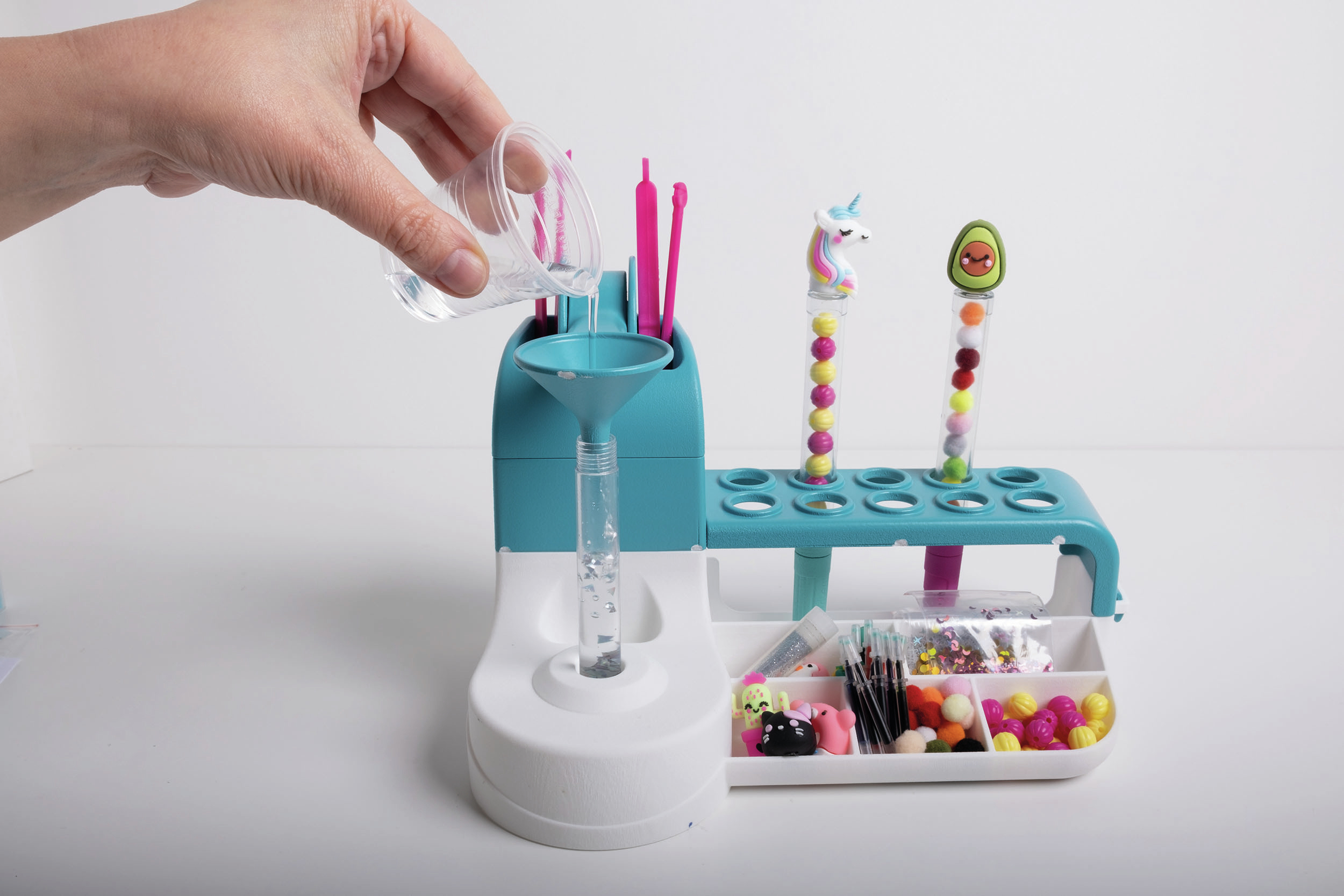 Una mano versa liquido in un imbuto su una stazione artigianale con perline e figure.