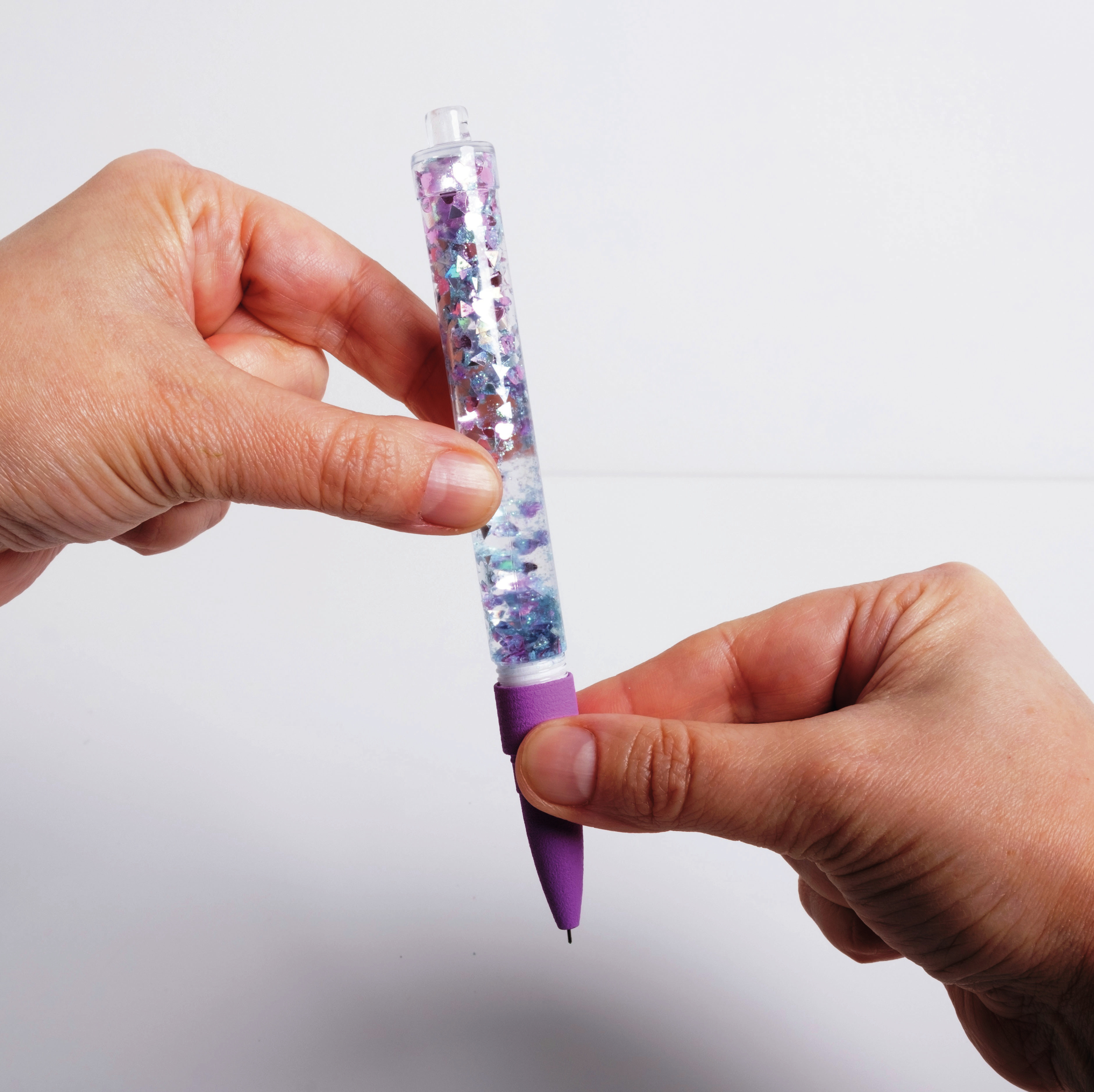 Mani che tengono una penna trasparente con glitter viola e forme di farfalla.