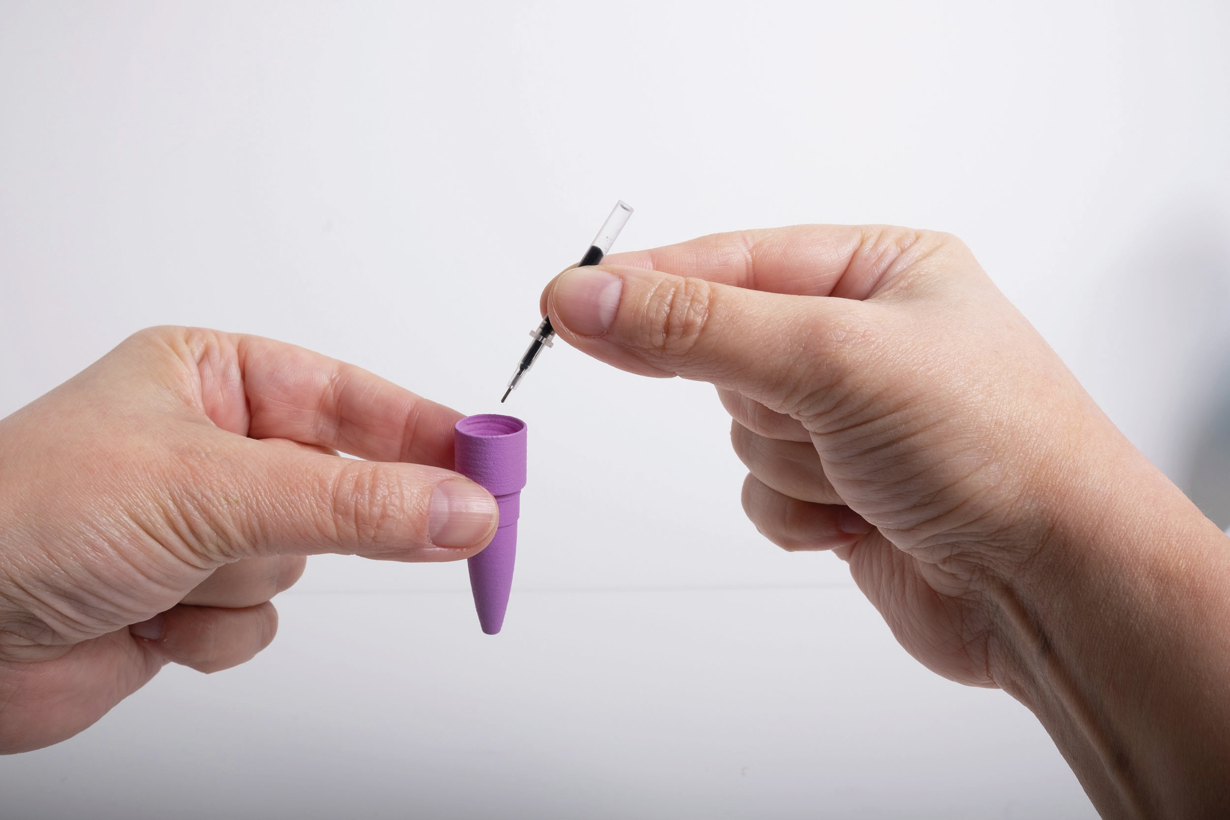 Una mano tiene una siringa sopra un contenitore viola.