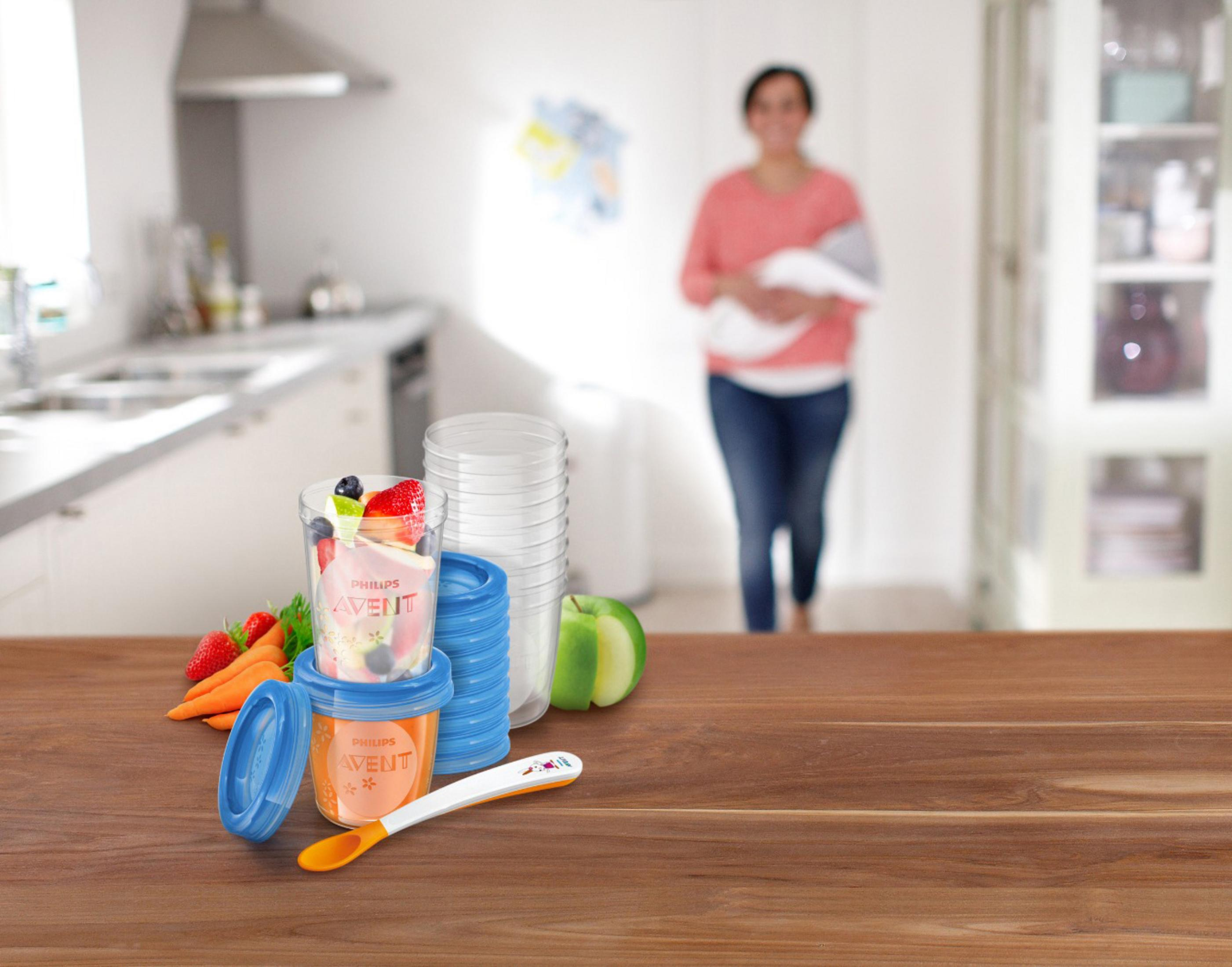 Babykostbehälter mit Früchten, Karotten, Apfel und Löffel auf Holztisch.