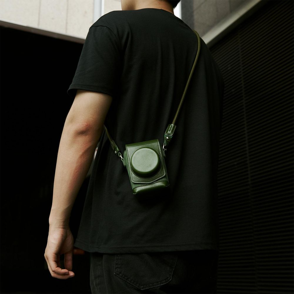 Man met zwart t-shirt en jeans, met groene leren cameratas schuin over het lichaam.