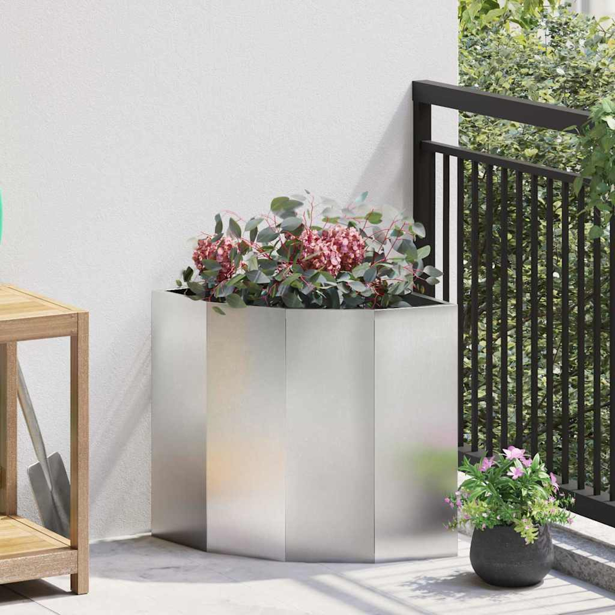 Un fioriera argentata con fiori rosa e foglie verdi su un balcone.