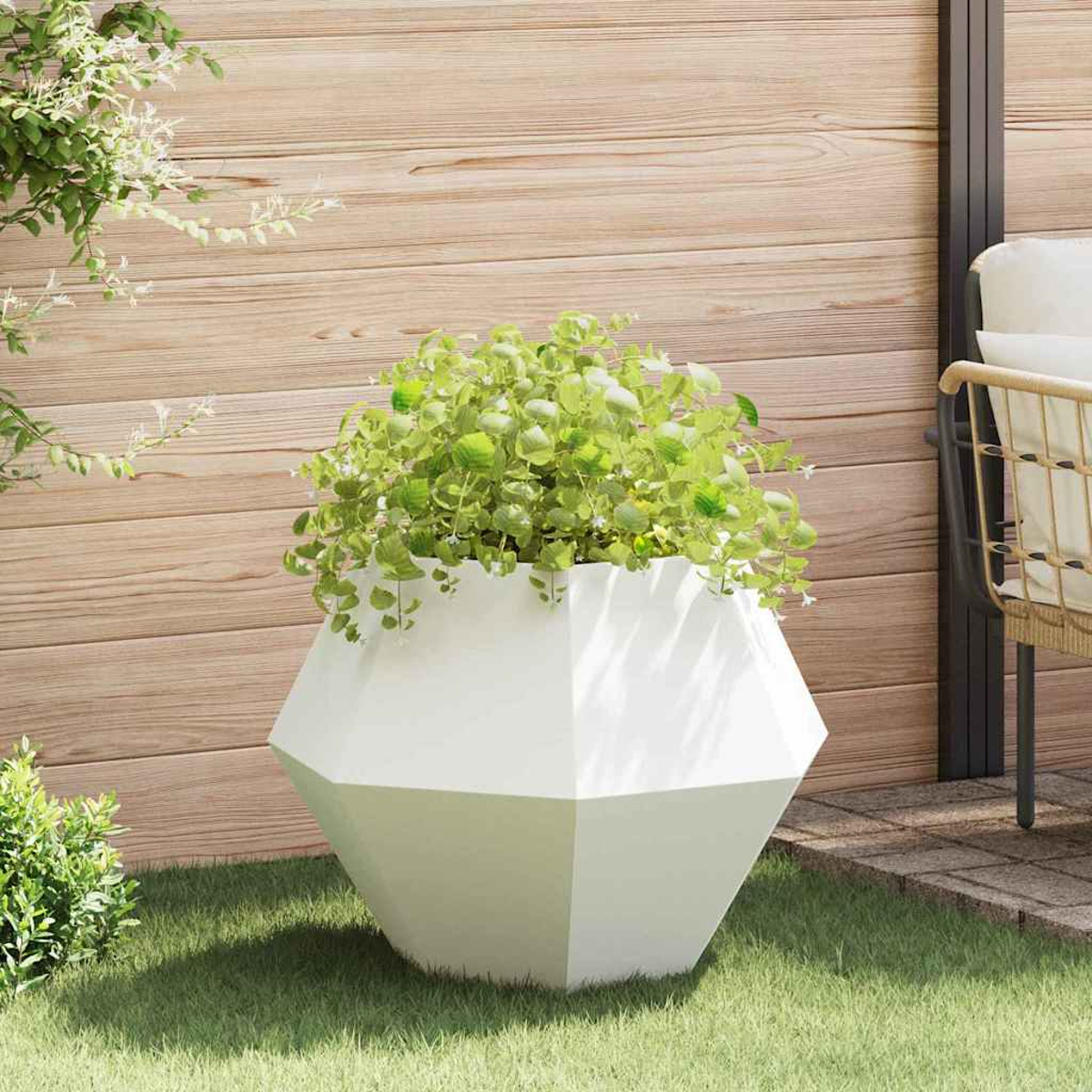 Un vaso geometrico bianco con piante verdi su erba davanti a una parete di legno.