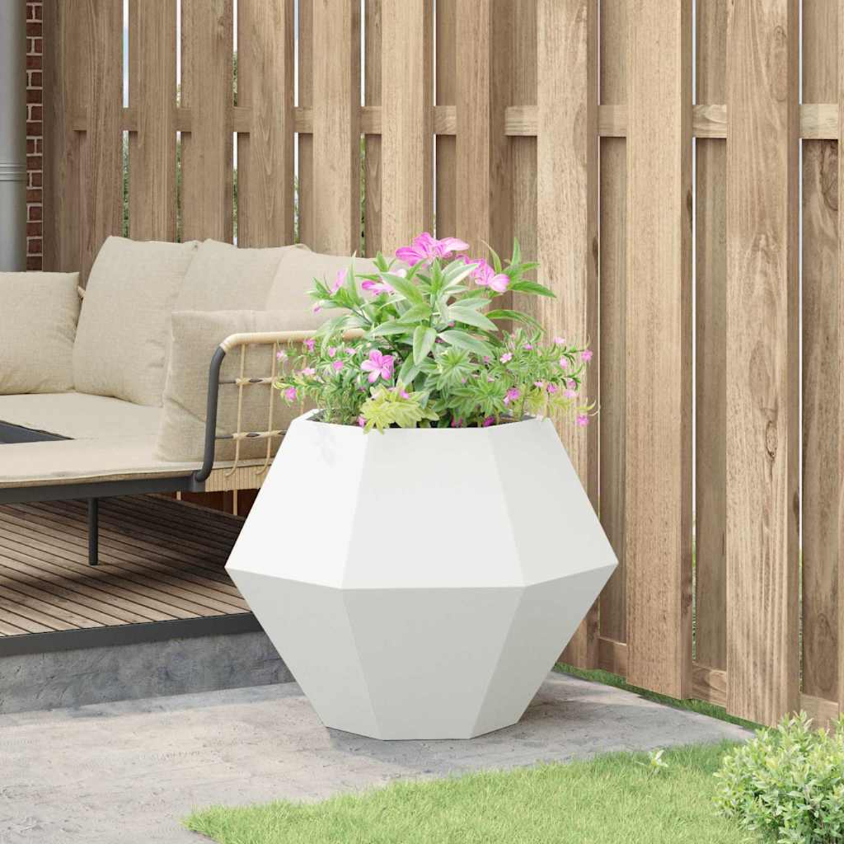 Una fioriera geometrica bianca con fiori rosa si trova su un patio vicino a un divano.