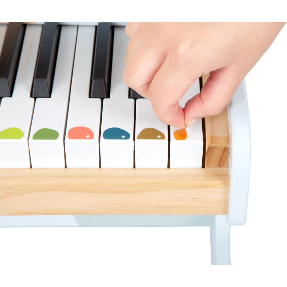 Una mano toca la tecla naranja de un piano de madera con notas de colores.