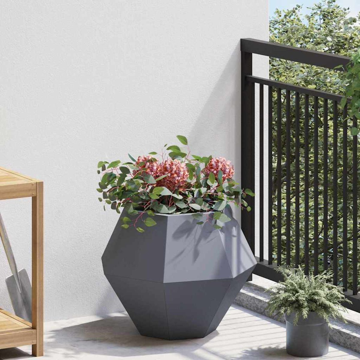 Una fioriera geometrica grigia con fiori rosa e foglie verdi si trova su un balcone.