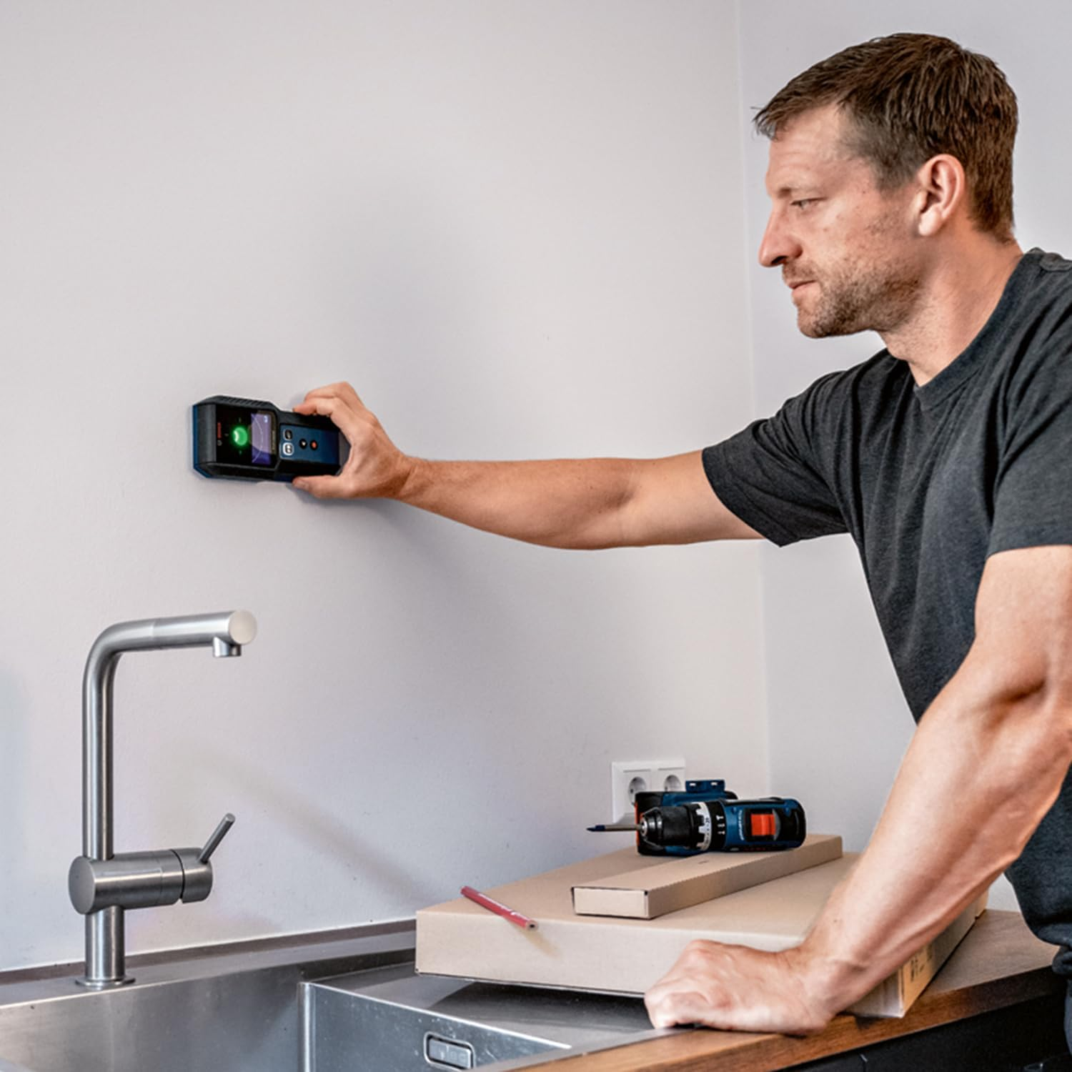 Uomo usa scanner muro vicino lavello cucina; attrezzi su scatole.